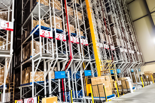 Pallet AS/RS with a stacker crane, high-bay racks, and pallets on the inbound conveyor